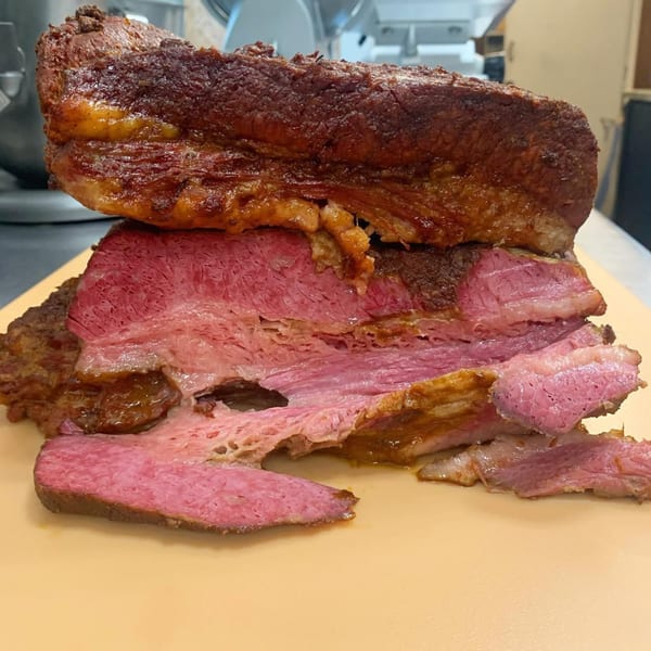 A large, juicy cut of corned beef, partially sliced, revealing its pink interior and crispy exterior.