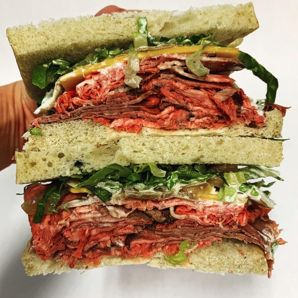 A towering, sliced roast beef sandwich from The Depot, filled with meat, cheese, lettuce, and sauce.