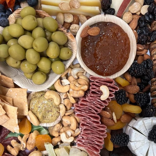 A charcuterie board with olives, cheeses, nuts, dried fruits, crackers, and dips.